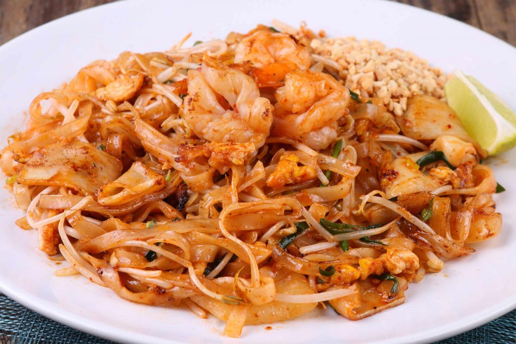 A plate of Pad Thai with prawns, squid, bean sprouts, crushed peanuts and a wedge of lime. An iconic Thai Food.