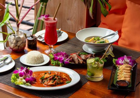 A colourful spread of Thai dishes, rice and drinks served on a wooden table.