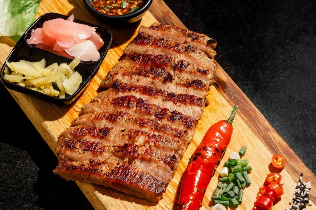 A steak and aromatics on a wooden chopping board.