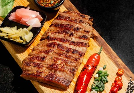A steak and aromatics on a wooden chopping board.
